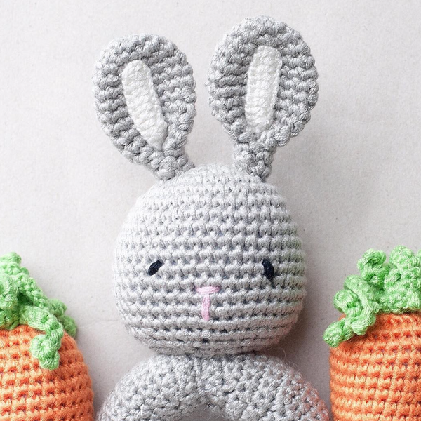Crocheted gray bunny with carrot toys on a light background