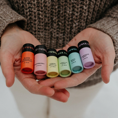 Hands holding a row of colorful lip balm containers with visible brand names.