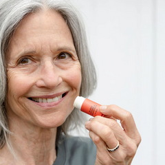 Woman holding a lip balm and smiling against a white background