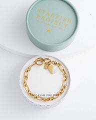 Gold bracelet with a tag in a 'Starfish Project' box on a white background