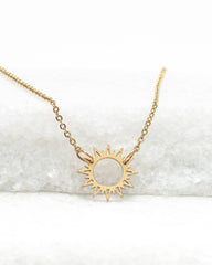 Gold sun-shaped pendant necklace on a white background
