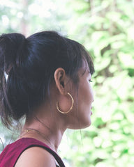 Woman wearing gold hoop earrings with a blurred green background
