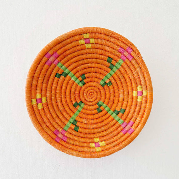 Round woven basket with orange base and colorful patterns on a white background
