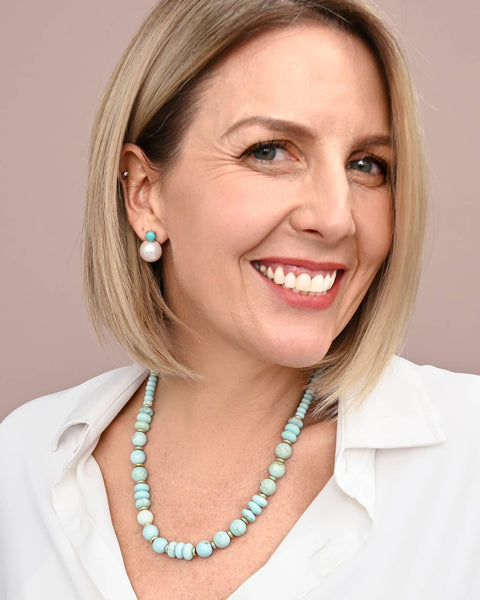 Woman wearing a white shirt and turquoise necklace against a beige background
