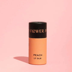 Peach lip balm with black cap on a pink background
