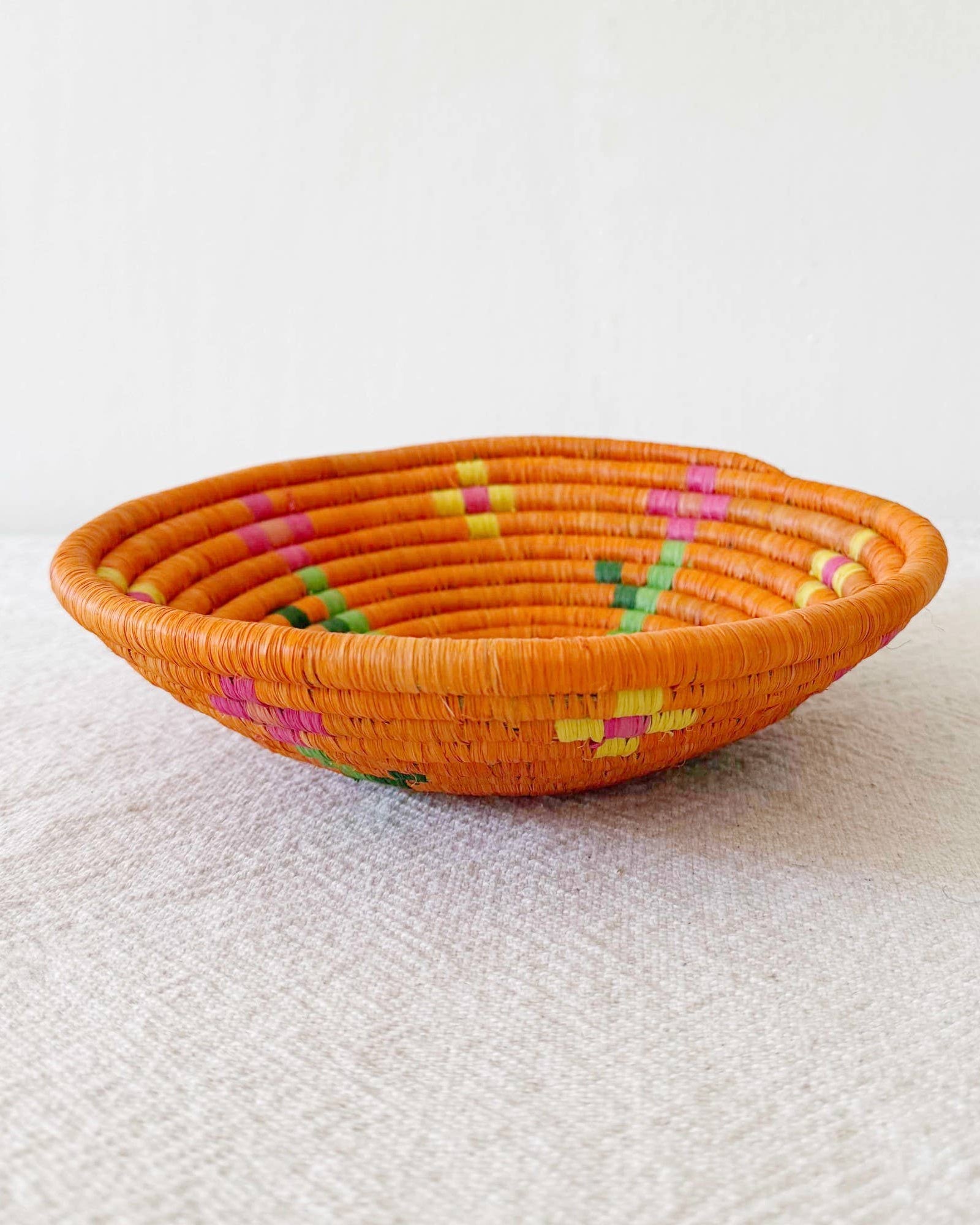 Orange woven basket with colorful patterns on a white surface