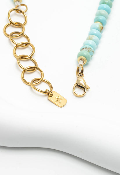 Gold chain necklace with a tag and turquoise beaded necklace on a white background