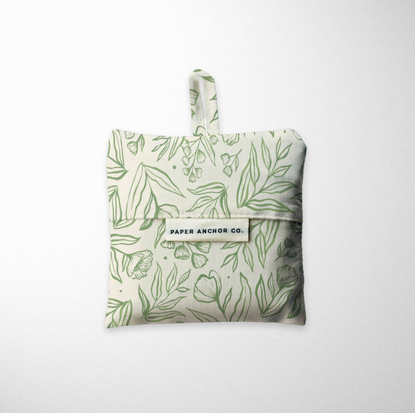 Folded reusable shopping bag with green leaf pattern on a white background