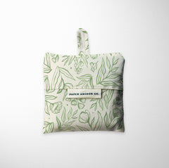 Folded reusable shopping bag with green leaf pattern on a white background