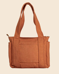 A terracotta orange canvas tote bag with dual shoulder straps and a front pocket, photographed against a neutral light gray background.