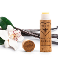 Bee Bella lip balm with wooden cap and bamboo container on a white background with vanilla beans and flowers.