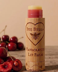 Bee Bella lip balm with wooden container on a wooden surface with cherries in the background