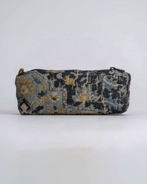 A rectangular zippered pouch with a woven, distressed tapestry pattern in navy blue, beige, and gold, shown against a plain light gray background.
