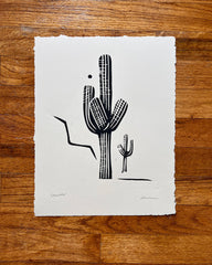 Black and white cactus illustration on a white paper sheet, placed on a wooden surface.