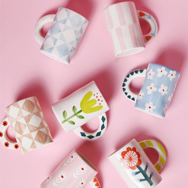 Set of colorful mugs with floral and geometric designs on a pink background