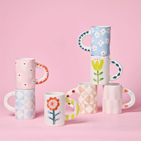 Set of colorful mugs with floral and geometric designs on a pink background