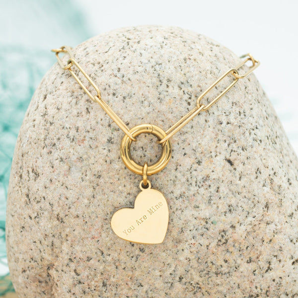 Gold necklace with a heart pendant on a textured stone surface