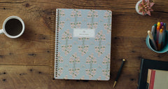 Notebook with floral pattern on a wooden desk with coffee and stationery items