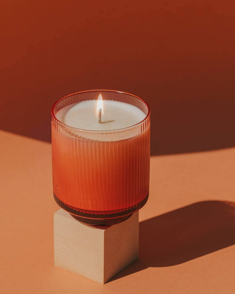 Candle in a red glass holder on a brown surface with a warm color palette