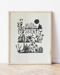 Framed black and white artwork of desert plants on a light wooden floor.