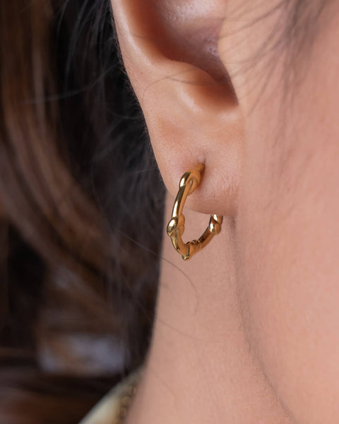 A close-up shot of a person's ear wearing a polished gold huggie hoop earring.