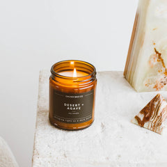 Candle labeled 'Desert Agave' on a textured surface with decorative stones.