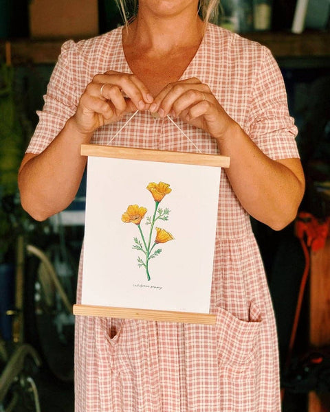 Person holding a small framed artwork with a floral design.