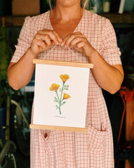 Person holding a small framed artwork with a floral design.