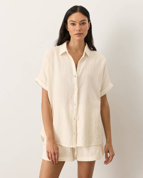 Woman wearing a beige button-up shirt and shorts on a white background