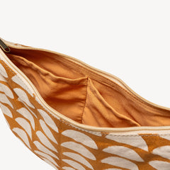 Close-up of an open zip pouch showing a warm orange-brown interior lining and a patterned exterior with white leaf-like shapes on a mustard-brown base.
