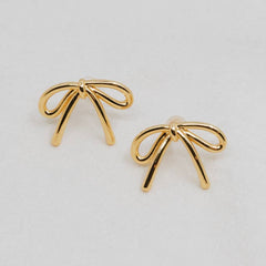 Gold bow-shaped earrings on a light gray background