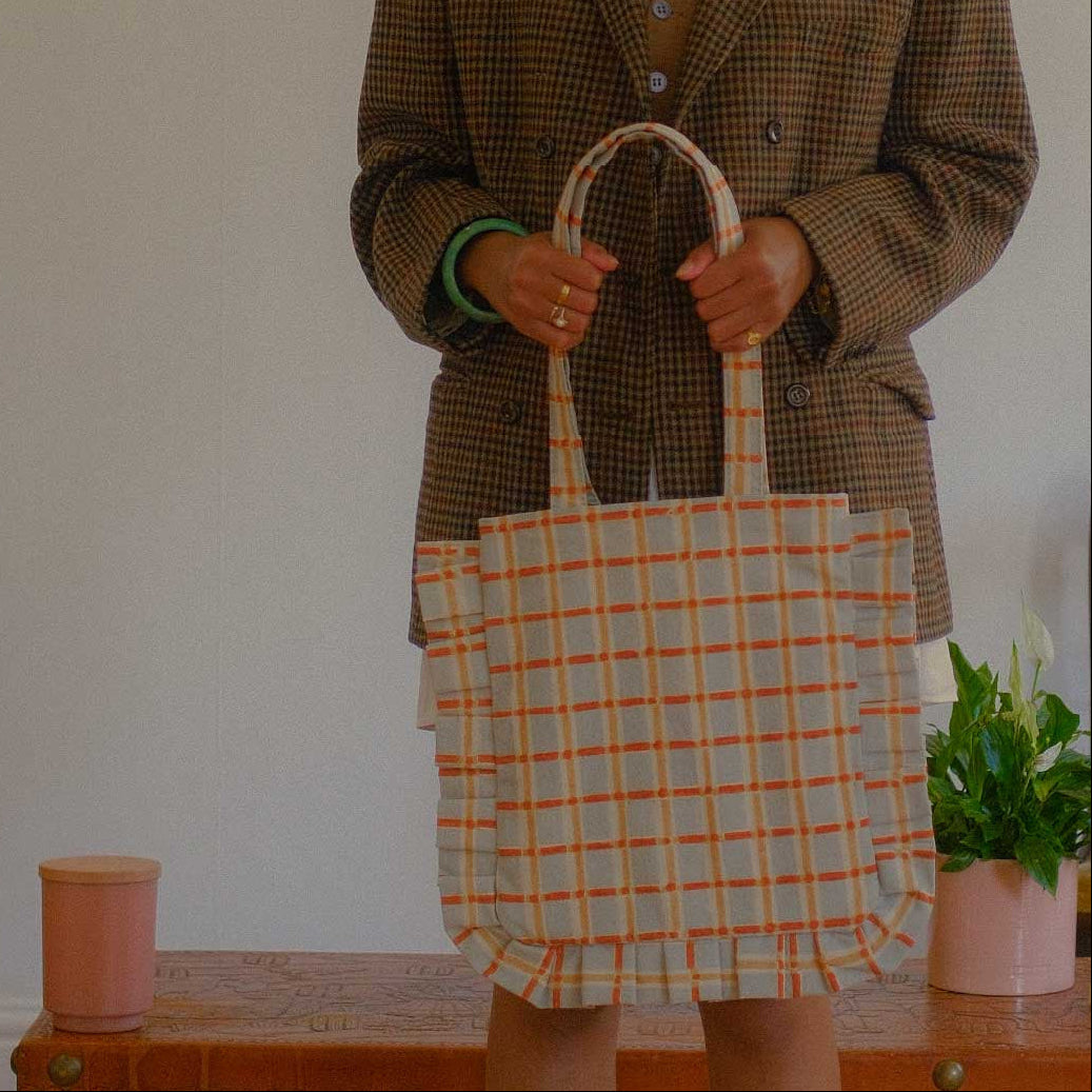 Person holding a plaid tote bag in a room with a plant and candle.