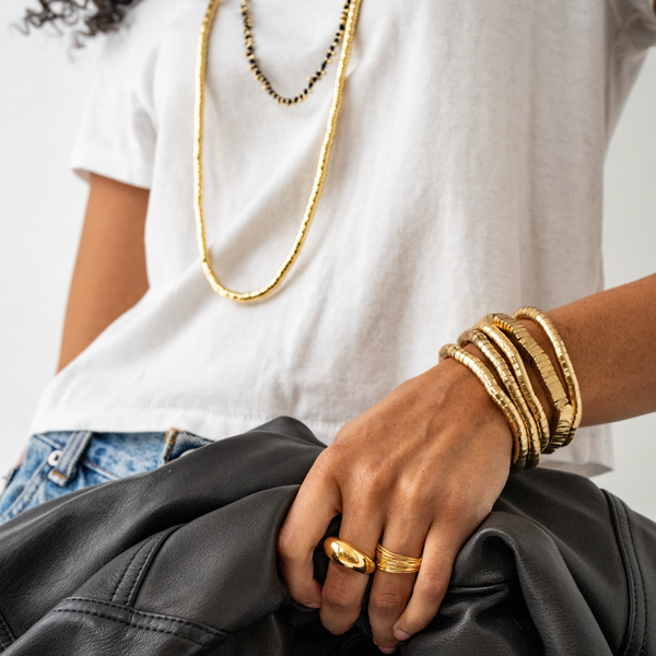 Person wearing gold jewelry including necklaces, bracelets, and a ring on a white background