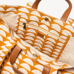 Close-up of the interior of a tote bag with a mustard yellow and cream scallop pattern, tan leather handles, and a zippered pocket.