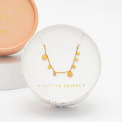 Gold necklace in a clear display case with 'Starfish Project' branding on a light background