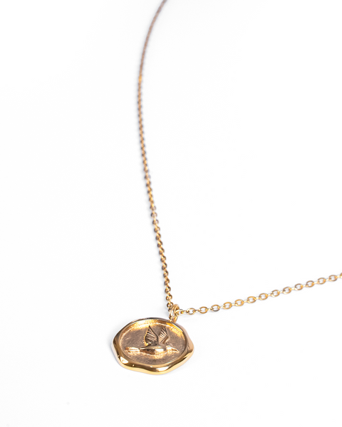 A delicate gold chain necklace featuring a small, irregularly shaped gold pendant with an embossed bird, set against a plain white background.