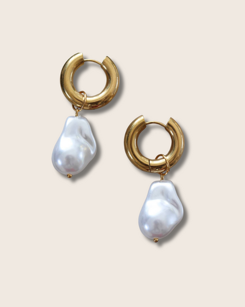 Gold hoop earrings with baroque pearl drops on a beige background