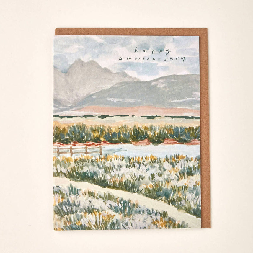Greeting card with mountain landscape illustration and 'happy anniversary' text on a beige background