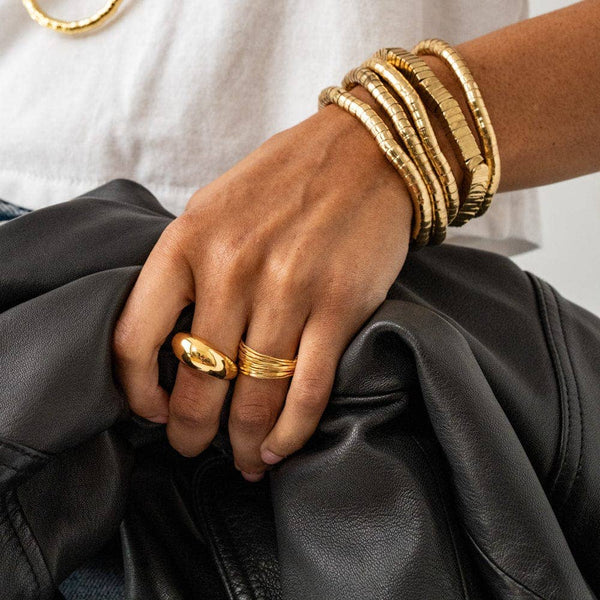 Hand wearing gold rings and bracelets on a black leather surface