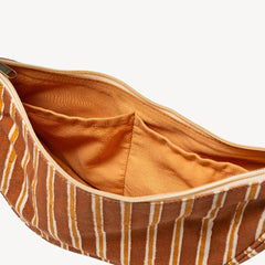 Close-up of an open striped fabric pouch showing a warm orange-brown interior lining and a matching zipper track, with the exterior fabric featuring vertical stripes in brown, orange, and cream on a light gray background.