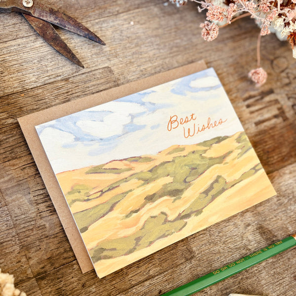 Greeting card with landscape design on a wooden surface with flowers and a pencil.