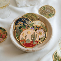 Decorative coasters with desert-themed designs in a bowl on a white surface.
