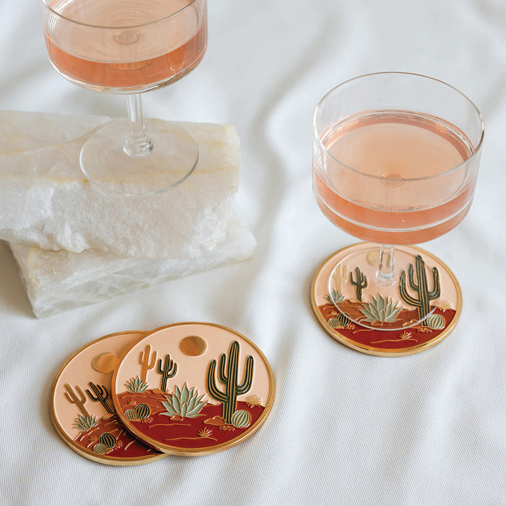 Coasters with cactus design on a white surface with glasses of pink drink.