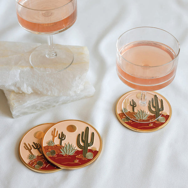 Coasters with cactus design on a white surface with glasses of pink drink.