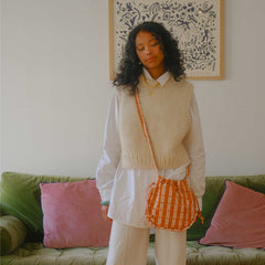 Woman standing in a room with a green couch and pink pillows, holding an orange checkered bag.