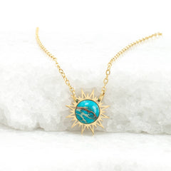 Gold necklace with a turquoise sun pendant on a white marble surface