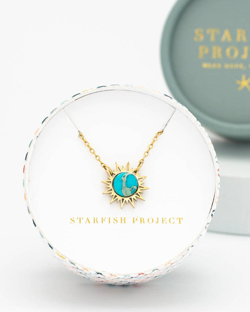 Gold necklace with a turquoise pendant in a Starfish Project box on a white background
