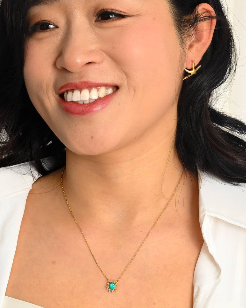Woman wearing a gold necklace with a turquoise pendant against a white background