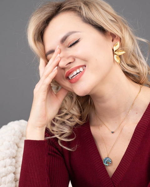 Woman wearing a red sweater and gold earrings with a gray background