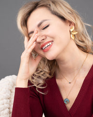 Woman wearing a red sweater and gold earrings with a gray background